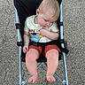 baby, child, toddler, sleeping, stroller, outdoor, pavement, clothing, shorts, tshirt, barefoot, metal, black_fabric, seatbelt, head, legs, feet, person, resting, peaceful