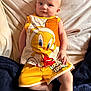 baby, child, infant, toddler, person, clothing, yellow_shorts, looney_tunes, tweety_bird, blanket, fabric, couch, relaxing, indoors, cute, portrait, smiling, skin, head, face