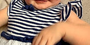 Abby is registered to the contest to win money with this photo: baby, child, smiling, striped_dress, blue_and_white, hand, face, person, infant, cute, lying_down, soft_background, playful, young_child, skin, eyes, apparel, portrait, happy, indoors