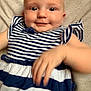 baby, child, smiling, striped_dress, blue_and_white, hand, face, person, infant, cute, lying_down, soft_background, playful, young_child, skin, eyes, apparel, portrait, happy, indoors
