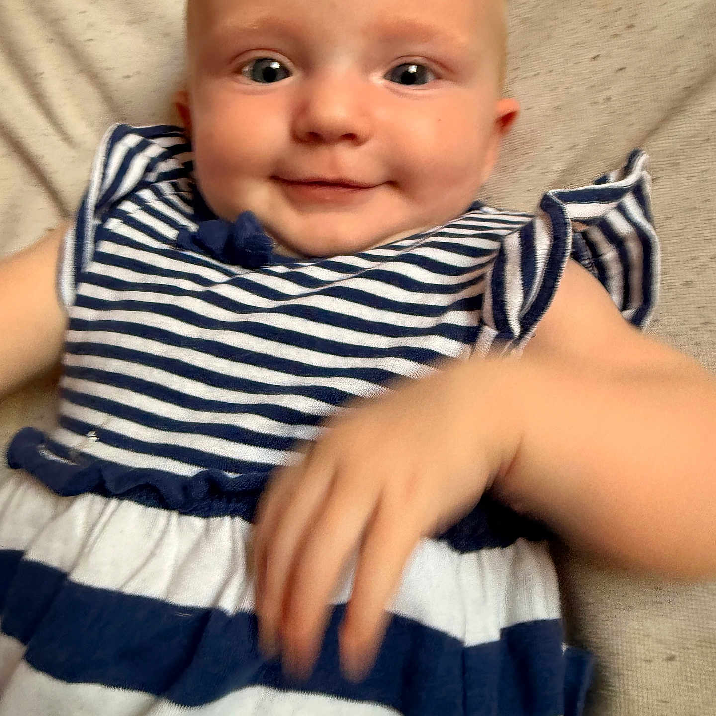 Abby is registered to the contest to win money with this photo: apparel, baby, blue_and_white, child, cute, eyes, face, hand, happy, indoors, infant, lying_down, person, playful, portrait, skin, smiling, soft_background, striped_dress, young_child