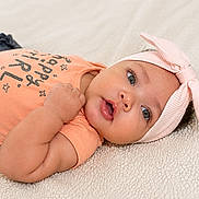 Calissia is registered to the contest to win money with this photo: baby, infant, child, headband, bow, peach_shirt, happy_girl_text, lying_down, soft_blanket, cute, portrait, face, eyes, hand, skin, clothing, indoors, young_child, adorable, expression