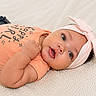 baby, infant, child, headband, bow, peach_shirt, happy_girl_text, lying_down, soft_blanket, cute, portrait, face, eyes, hand, skin, clothing, indoors, young_child, adorable, expression