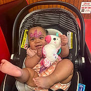 Wynter joined the competition — help win amazing prizes! baby, car_seat, face_paint, plush_toy, unicorn, child, smiling, indoor, wood_paneling, red_wall, foot, clothing, seatbelt, person, cute, happy, infant, toy, portrait, booth