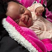 Wynter is registered to the contest to win money with this photo: baby, blanket, pink, smiling, happy, infant, curly_hair, cozy, soft_texture, sleepwear, portrait, child, indoors, candid, cute, warm, comfort, face, expression, resting