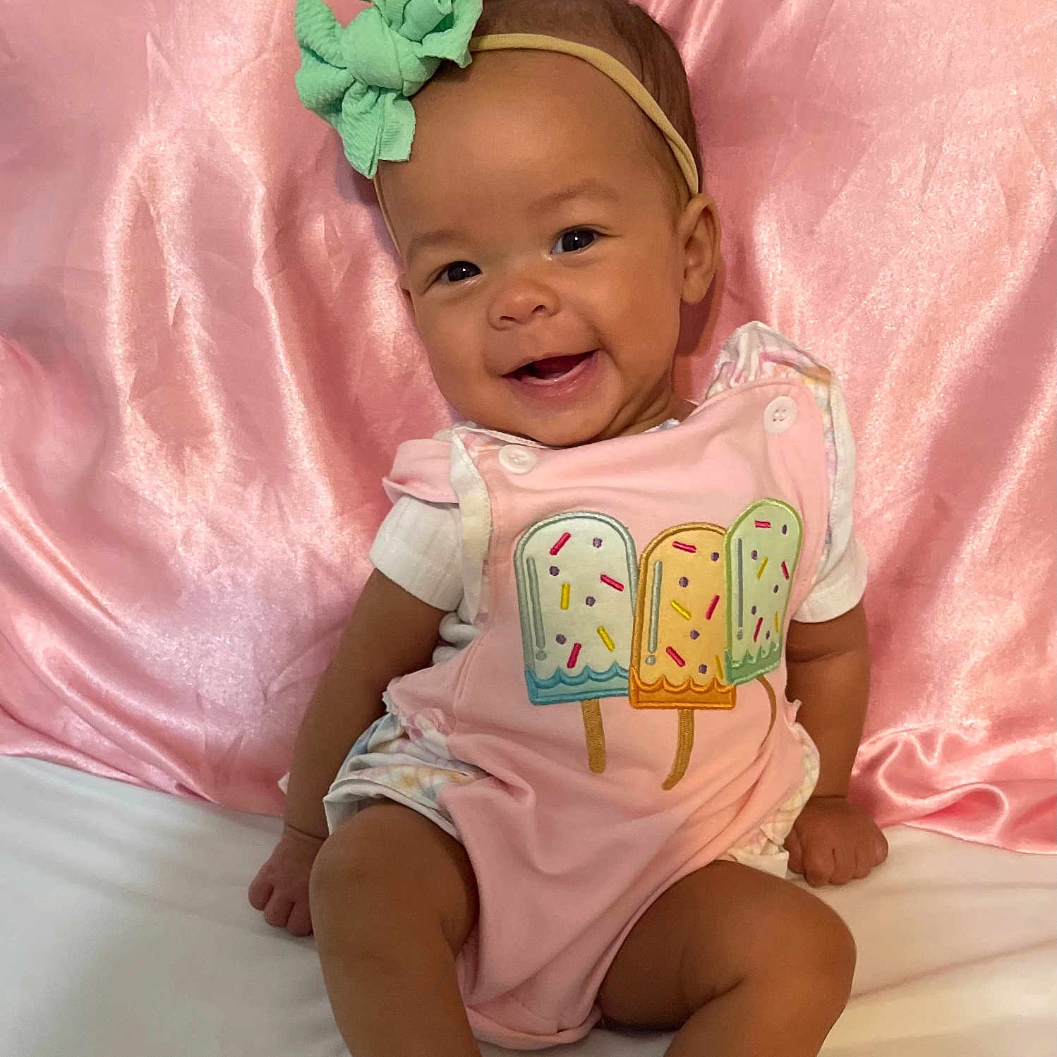 Paisley joined the competition — help win amazing prizes! baby, child, smiling, headband, green_bow, pink_outfit, popsicle_design, sitting, white_socks, pink_satin_backdrop, cute, happy, portrait, indoor, infant, person, apparel, fashion, baby_clothes, soft_texture