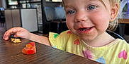Barbara is registered to the contest to win money with this photo: toddler, child, smiling, face, blue_eyes, eating, food, table, wood, indoor, restaurant, high_chair, clothing, short_hair, earrings, window, daylight, happy, person, casual