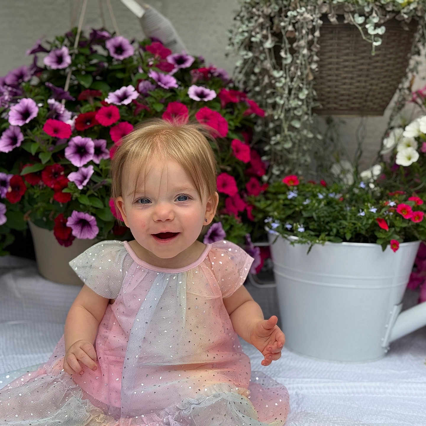Barbara is registered to the contest to win money with this photo: baby, blanket, child, cute, dress, face, flowers, garden, greenery, happy, indoor, pink, portrait, potted_plants, purple, sitting, smiling, toddler, watering_can, white