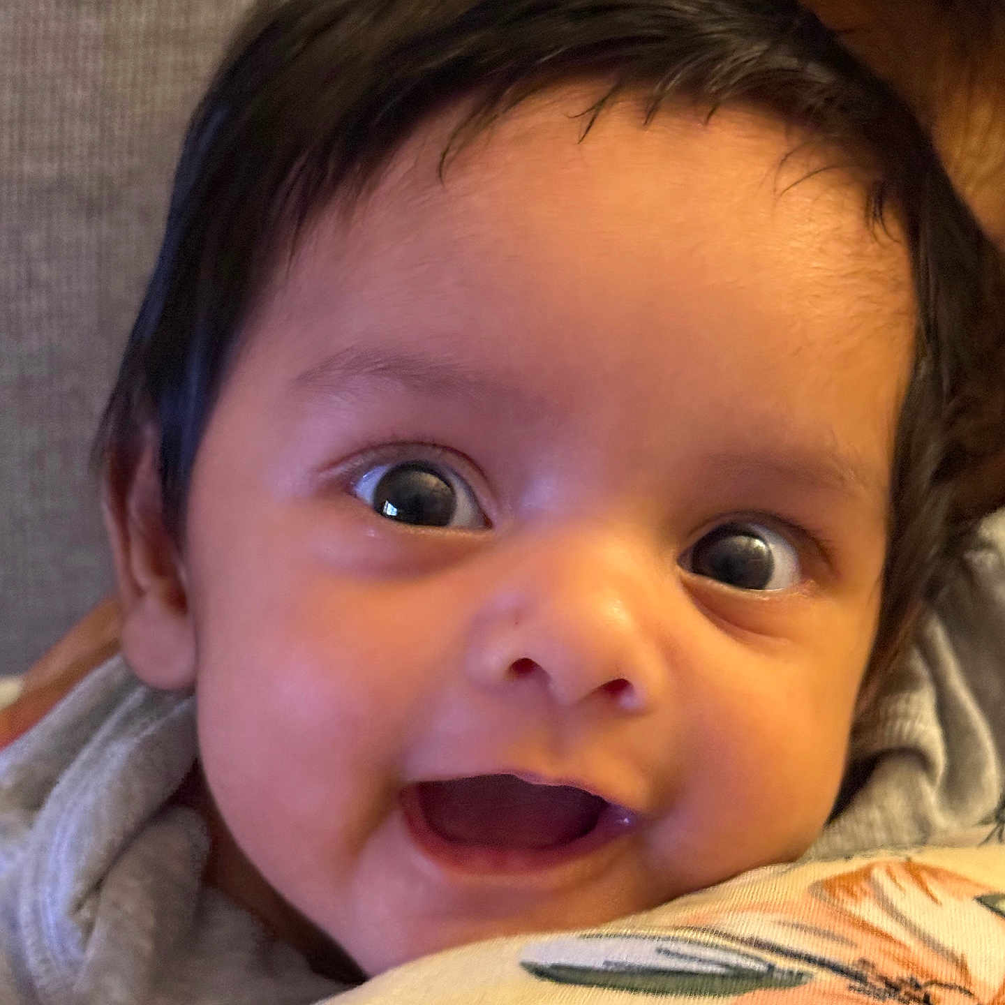 Mehsan is registered to the contest to win money with this photo: baby, child, close_up, cozy, cute, dark_hair, expression, eyes, face, floral_pattern, happy, indoors, infant, person, pillow, portrait, resting, smile, soft_background, young
