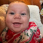Jaiven is registered to the contest to win money with this photo: baby, smiling, face, closeup, blanket, red, green, white, pattern, cozy, indoor, infant, cute, happy, person, plush, texture, soft, portrait, child
