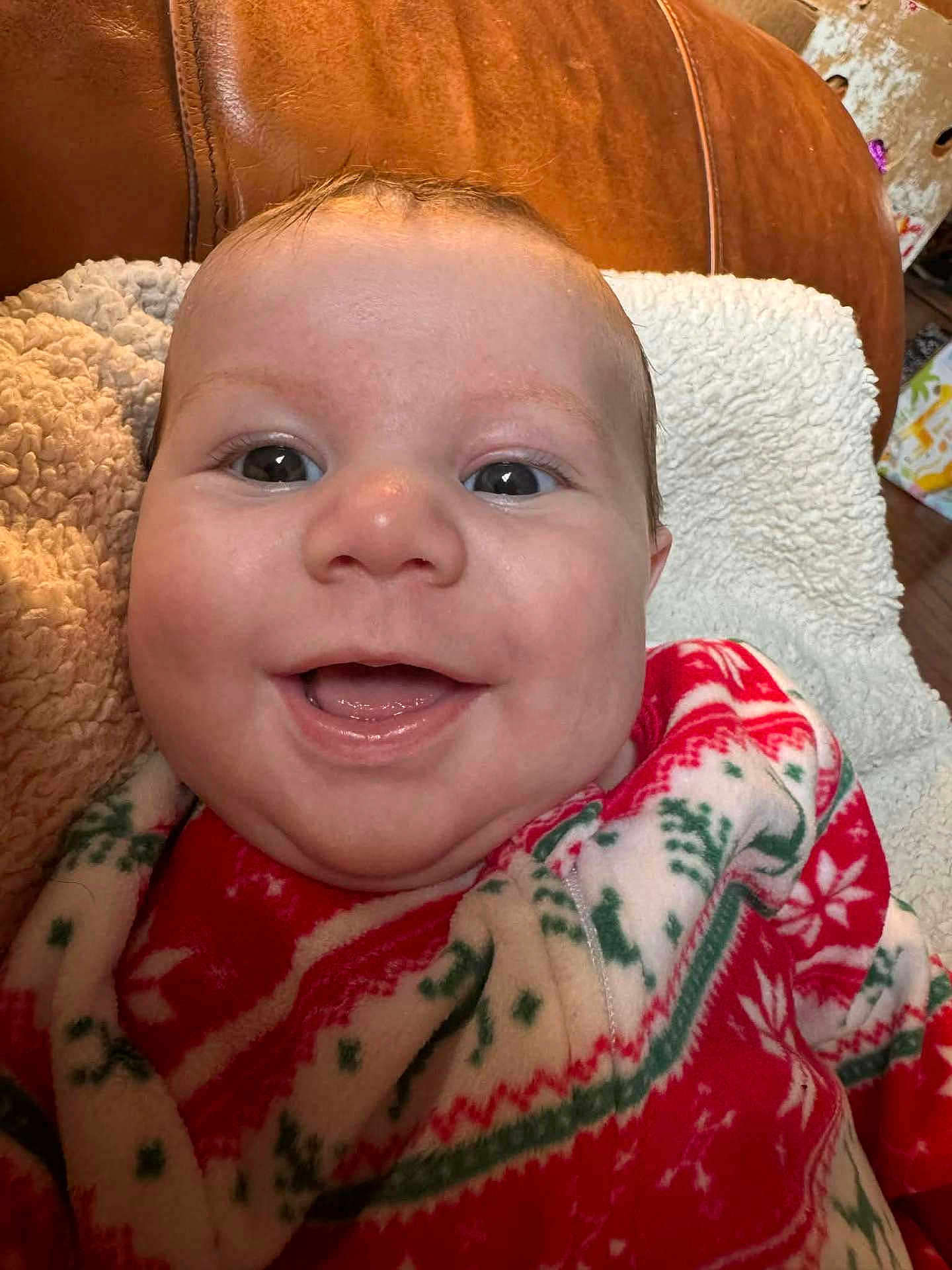 Jaiven is registered to the contest to win money with this photo: baby, smiling, face, closeup, blanket, red, green, white, pattern, cozy, indoor, infant, cute, happy, person, plush, texture, soft, portrait, child