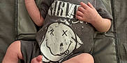 Albie is registered to the contest to win money with this photo: baby, infant, child, tshirt, nirvana, smiley_face, lying_down, mat, padded_mat, barefoot, skin, head, arms, legs, hand, foot, face, looking_away, clothing, indoors