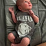 Albie is registered to the contest to win money with this photo: baby, infant, onesie, nirvana, clothing, lying_down, gray_mat, skin, legs, arms, face, head, expression, cute, newborn, indoors, soft_texture, looking_up, barefoot, human