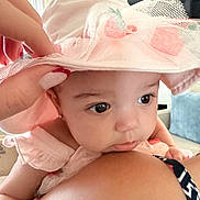 Alina is registered to the contest to win money with this photo: baby, child, pink_hat, netting, flower, curious, close_up, tattoo, manicured_nails, indoor, soft_light, face, person, holding, shoulder, cute, infant, skin, portrait, expression
