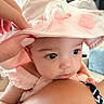 baby, child, pink_hat, netting, flower, curious, close_up, tattoo, manicured_nails, indoor, soft_light, face, person, holding, shoulder, cute, infant, skin, portrait, expression