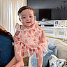 baby, child, smiling, dress, pink, living_room, couch, pillows, television, curtains, person, holding, happy, interior, furniture, decor, portrait, cute, indoor, toddler