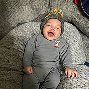 Kamari is registered to the contest to win money with this photo: baby, child, smiling, laughing, pajamas, hat, pom_pom, couch, quilted_cushion, cozy, indoor, person, happy, infant, clothing, relaxed, cute, home, seated, soft