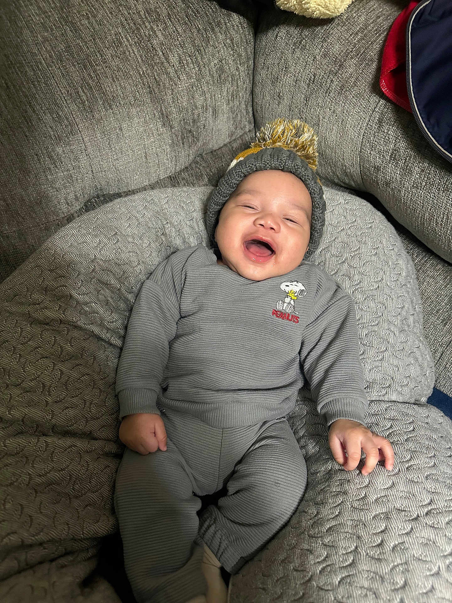 Kamari is registered to the contest to win money with this photo: baby, child, smiling, laughing, pajamas, hat, pom_pom, couch, quilted_cushion, cozy, indoor, person, happy, infant, clothing, relaxed, cute, home, seated, soft