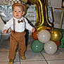 toddler, child, birthday, balloon, number_one, party, suspenders, brown_pants, hat, tile_floor, cup_stack, hedgehog_balloon, celebration, indoors, footwear, white_shirt, bow_tie, decorations, gift_wrap, hand