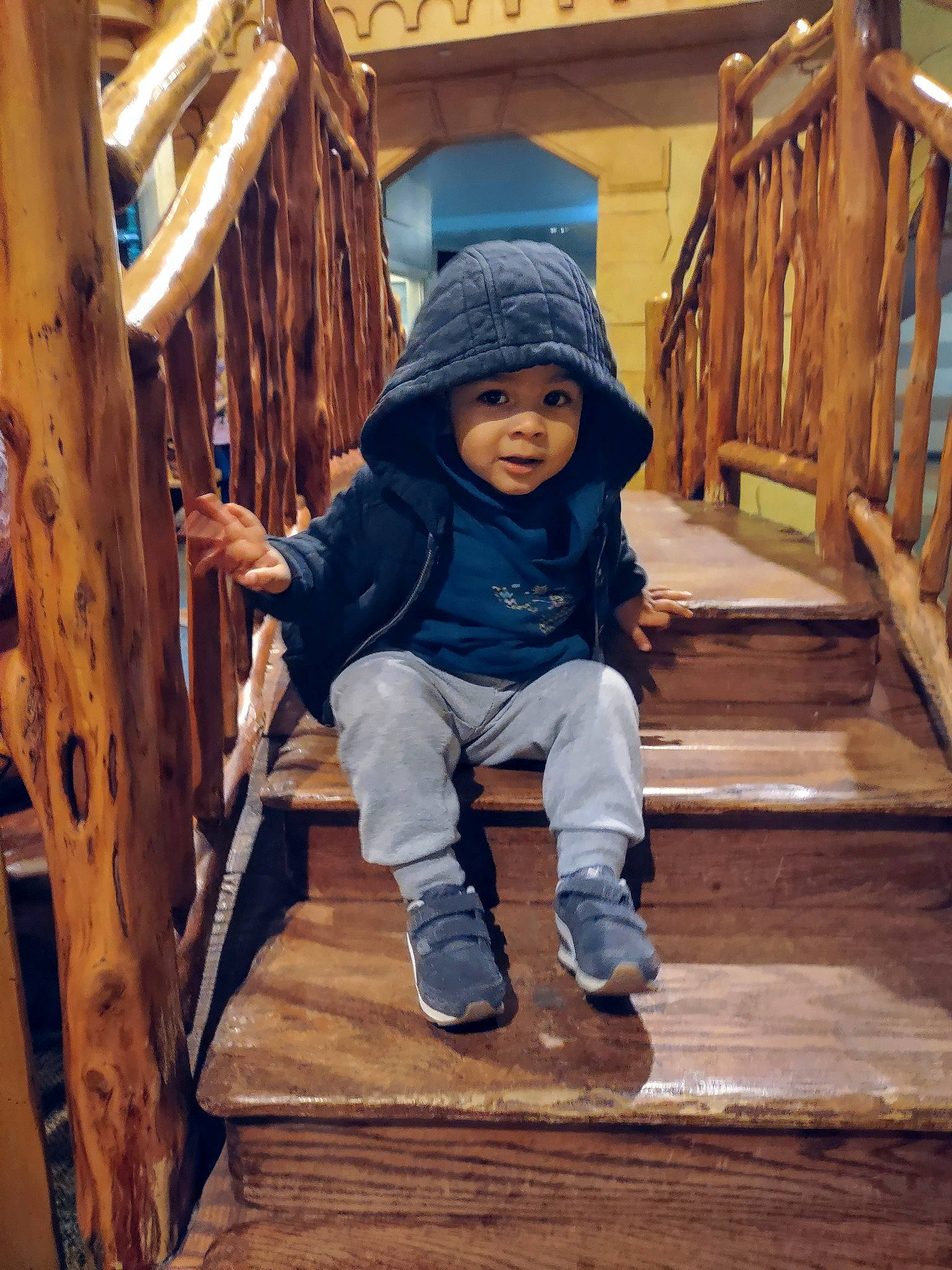Javon is registered to the contest to win money with this photo: child, comfort, facial_expression, fun, hardwood, hat, headwear, hoodie, house, jacket, leisure, log_cabin, person, play, shoe, sitting, smile, toddler, tree, winter