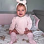 baby, child, smiling, pink_clothing, headband, bow, knee_socks, crib, blanket, deer_pattern, floral_pattern, indoor, nursery, soft_lighting, portrait, cute, happy, sitting, infant, person