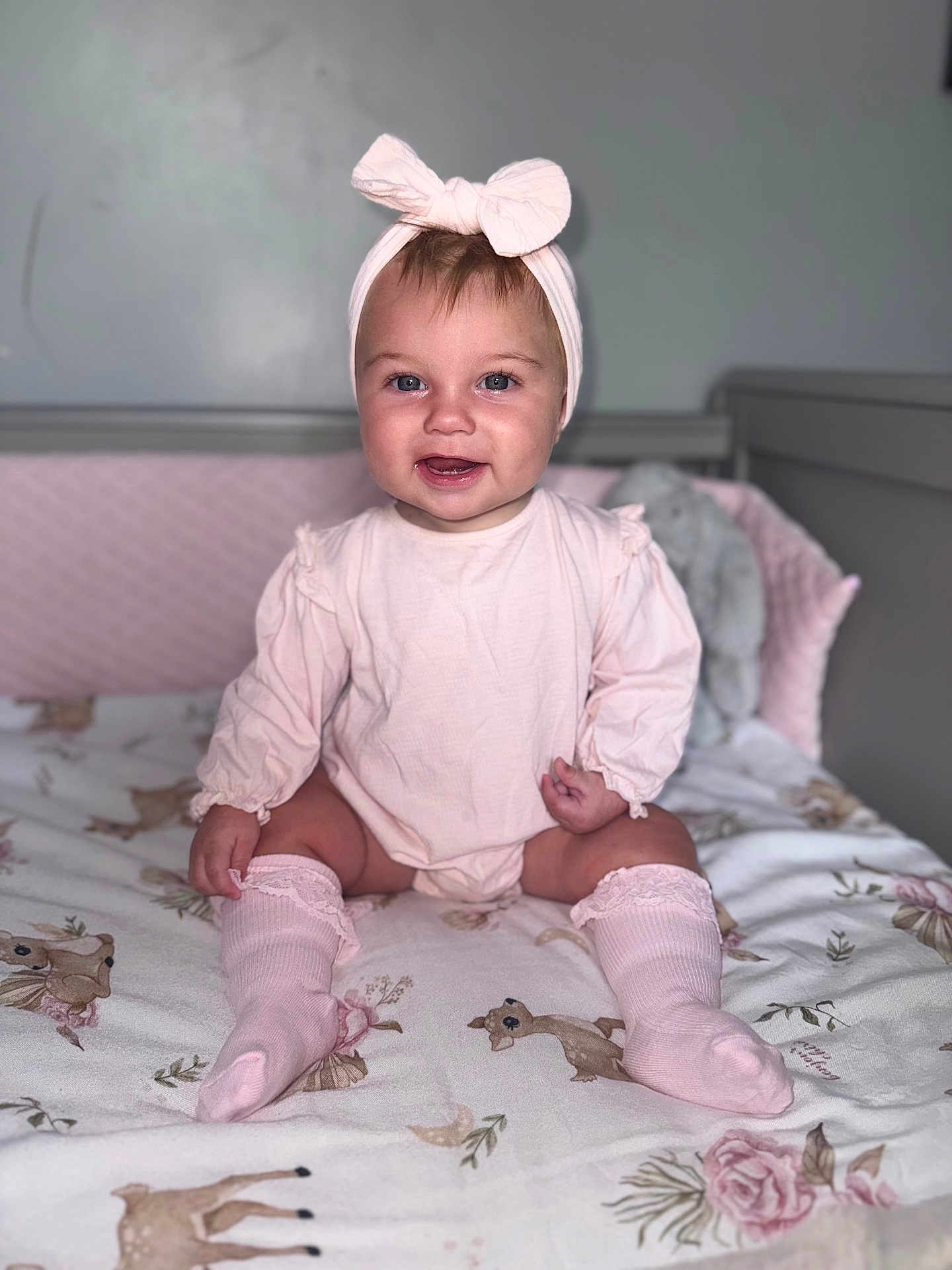 Ivy-Jean joined the competition — help win amazing prizes! baby, child, smiling, pink_clothing, headband, bow, knee_socks, crib, blanket, deer_pattern, floral_pattern, indoor, nursery, soft_lighting, portrait, cute, happy, sitting, infant, person