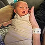 Parker is registered to the contest to win money with this photo: newborn, baby, swaddle, tattoo, arm, hospital_wristband, couch, baby_wipes, person, infant, resting, indoors, skin, hand, clothing, comfort, relaxation, wrapped, care, parent