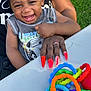 Tamir joined the competition — help win amazing prizes! toddler, child, smiling, curly_hair, sleeveless_shirt, adult_hand, red_nails, ring, outdoor, grass, table, toy_rings, colorful, happy, person, holding, lap, closeup, daylight, joy