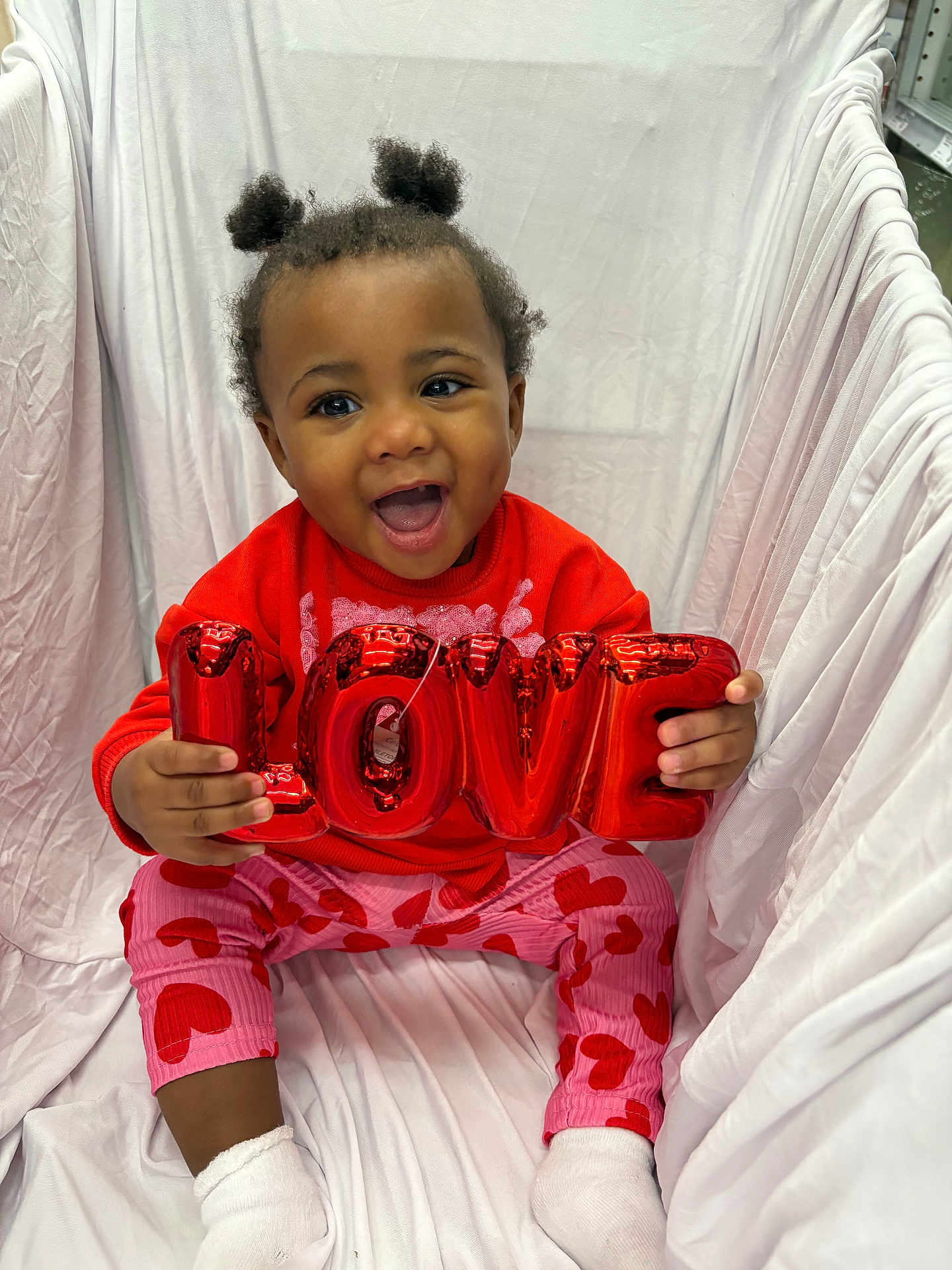 Elizabelle joined the competition — help win amazing prizes! toddler, child, smiling, love, balloon, red_sweater, pink_pants, heart_pattern, socks, indoor, white_background, happy, cute, portrait, seated, baby, puffy_hair, playful, colorful_clothing, joyful