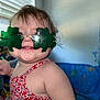 toddler, child, sunglasses, green, shamrock, smile, red_dress, floral_pattern, indoor, window_blind, toys, happy, cute, face, person, baby, playful, cheerful, light, portrait