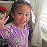 Diana is registered to the contest to win money with this photo: child, girl, smiling, waving, curly_hair, purple_dress, daisy_pattern, indoors, window, curtains, poinsettia, happy, portrait, young, cheerful, person, home, natural_light, earrings, joyful
