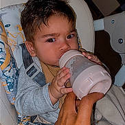 Kaëton a rejoint le concours — aidez-le/la à gagner de superbes lots ! baby, bottle, feeding, high_chair, cushion, hand, infant, child, face, eyes, clothing, seat_belt, indoor, person, holding, expression, nursery, care, comfort, young