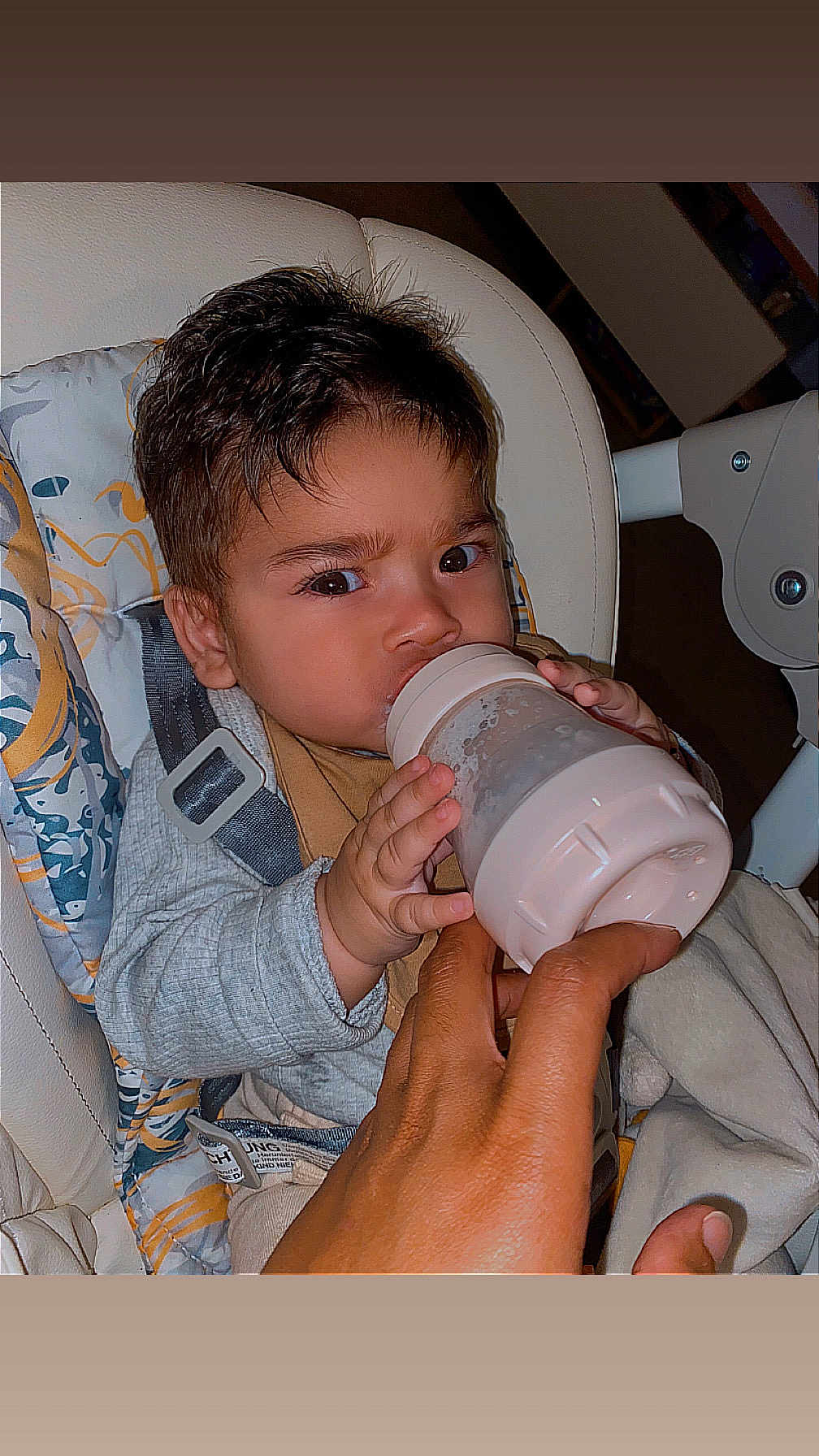 Kaëton a rejoint le concours — aidez-le/la à gagner de superbes lots ! baby, bottle, feeding, high_chair, cushion, hand, infant, child, face, eyes, clothing, seat_belt, indoor, person, holding, expression, nursery, care, comfort, young