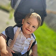 Sonnie-Lee joined the competition — help win amazing prizes! toddler, child, smile, stroller, outdoor, sunlight, grass, white_shirt, suspenders, happy, face, hands, portrait, baby, young_child, daylight, greenery, casual_clothing, closeup, cute