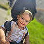 toddler, child, smile, stroller, outdoor, sunlight, grass, white_shirt, suspenders, happy, face, hands, portrait, baby, young_child, daylight, greenery, casual_clothing, closeup, cute