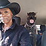 person, dog, car_interior, hat, fleece_jacket, earrings, smile, tongue_out, seat, collar, chain, window, sunlight, leather_seat, happy, pet, animal, vehicle, portrait, casual_wear