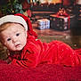 baby, infant, santa_hat, red_clothing, christmas, holiday, festive, blanket, face, blue_eyes, cute, indoors, decorations, gift_boxes, soft_lighting, portrait, toddler, holiday_season, cozy, smiling