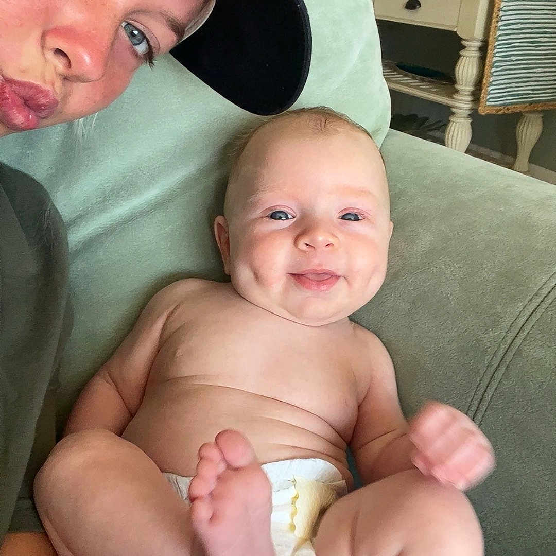 Krue Burgess is registered to the contest to win money with this photo: adult, baby, cap, casual, closeup, couch, diaper, dimples, face, furniture, green, happy, indoor, person, plant, room, seated, skin, smile, table