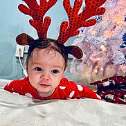 Alyssa is registered to the contest to win money with this photo: baby, child, reindeer_antlers, red_clothing, polka_dot, blanket, christmas_tree, presents, holiday, festive, indoors, cute, face, headband, smiling, toddler, soft_lighting, christmas_decorations, white_tree, floor