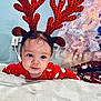 baby, child, reindeer_antlers, red_clothing, polka_dot, blanket, christmas_tree, presents, holiday, festive, indoors, cute, face, headband, smiling, toddler, soft_lighting, christmas_decorations, white_tree, floor