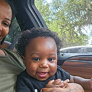 Syair Hayes joined the competition — help win amazing prizes! baby, child, adult, hand, tattoo, car_interior, window, trees, greenery, smile, happy, curly_hair, person, holding, clothing, seatbelt, portrait, daylight, skin, closeup