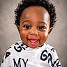 baby, black_text, child, closeup, clothing, curly_hair, cute, expression, eyes, face, happy, head, indoors, person, portrait, skin, smiling, toddler, white_shirt, young