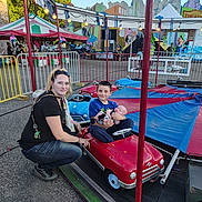 Lyric joined the competition — help win amazing prizes! carnival, amusement_park, child, baby, woman, miniature_car, ride, outdoor, smiling, family, tent, lights, fence, asphalt, daytime, casual_clothing, playful, fun, people, portrait