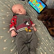 Nolan is registered to the contest to win money with this photo: baby, infant, mickey_mouse, onesie, bed, blanket, tablet, cartoon, dog, sleeping, pet, indoor, child, cute, clothing, pattern, resting, watching, technology, cozy