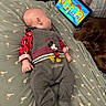 baby, infant, mickey_mouse, onesie, bed, blanket, tablet, cartoon, dog, sleeping, pet, indoor, child, cute, clothing, pattern, resting, watching, technology, cozy