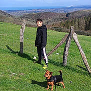 Pocket a rejoint le concours — aidez-le/la à gagner de superbes lots ! boy, casual_clothing, clouds, daytime, dog, fence, grass, greenery, happy, hill, landscape, leash, mountains, nature, outdoor, pet, scenery, sky, smiling, trees