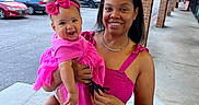 Sevyn joined the competition — help win amazing prizes! baby, infant, child, woman, mother, smiling, portrait, outdoor, pink_dress, pink_bow, baby_shoes, carrying, family, sidewalk, shopping_center, parking_lot, storefront, brick_columns, blue_sky, daylight