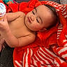 baby, child, blanket, red, white, striped, pout, cute, face, expression, hand, indoor, soft_lighting, cozy, person, infant, skin, toy, playful, warm