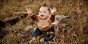 Wes is registered to the contest to win money with this photo: toddler, child, outdoor, grass, field, tree_stump, happy, smile, baby, nature, mohawk, casual_clothing, sitting, playful, autumn, young_child, person, joy, cute, raised_hands