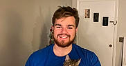 Jack Jack is registered to the contest to win money with this photo: beard, blue_shirt, boxes, carpet, casual, cat, door, feline, happy, holding, human, indoor, man, pet, portrait, room, short_hair, smiling, tabby_cat, wall
